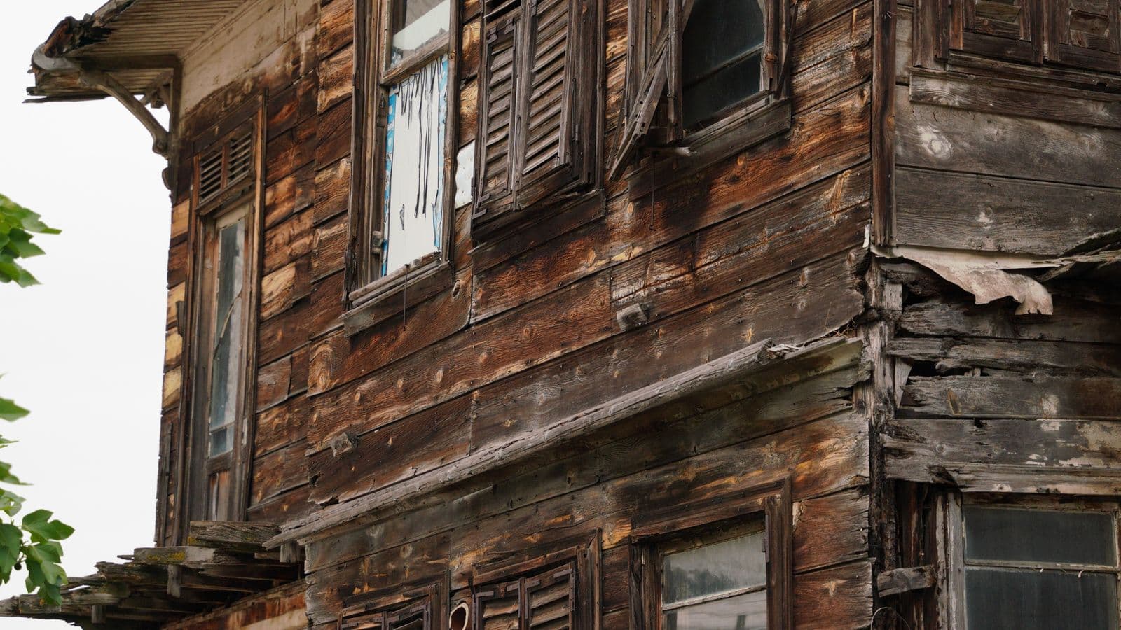 Weathered wooden house with damaged shutters and siding in need of major repairs
