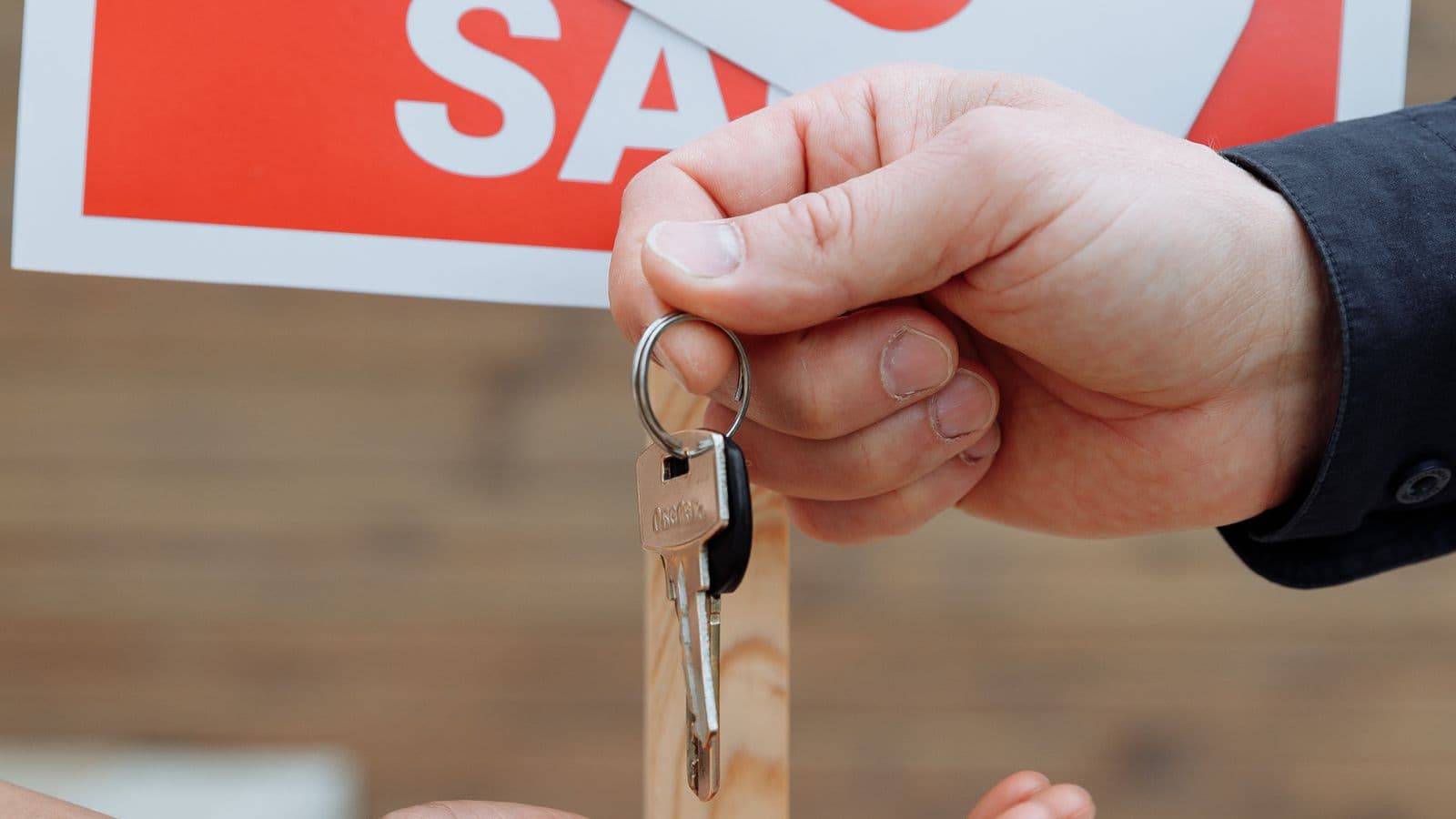 Seller handing over house keys in front of a sale sign after closing